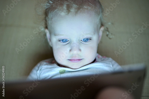 The little girl is fascinated by the screen of the tablet. The child is watching cartoons, front view