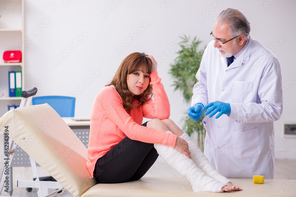 Fototapeta premium Young leg injured woman visiting old doctor traumatologist