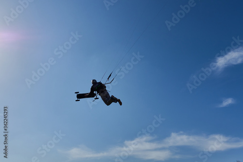 Man jumps through the air, holding in his hand an all terain board blue sky with white clouds. Germany.