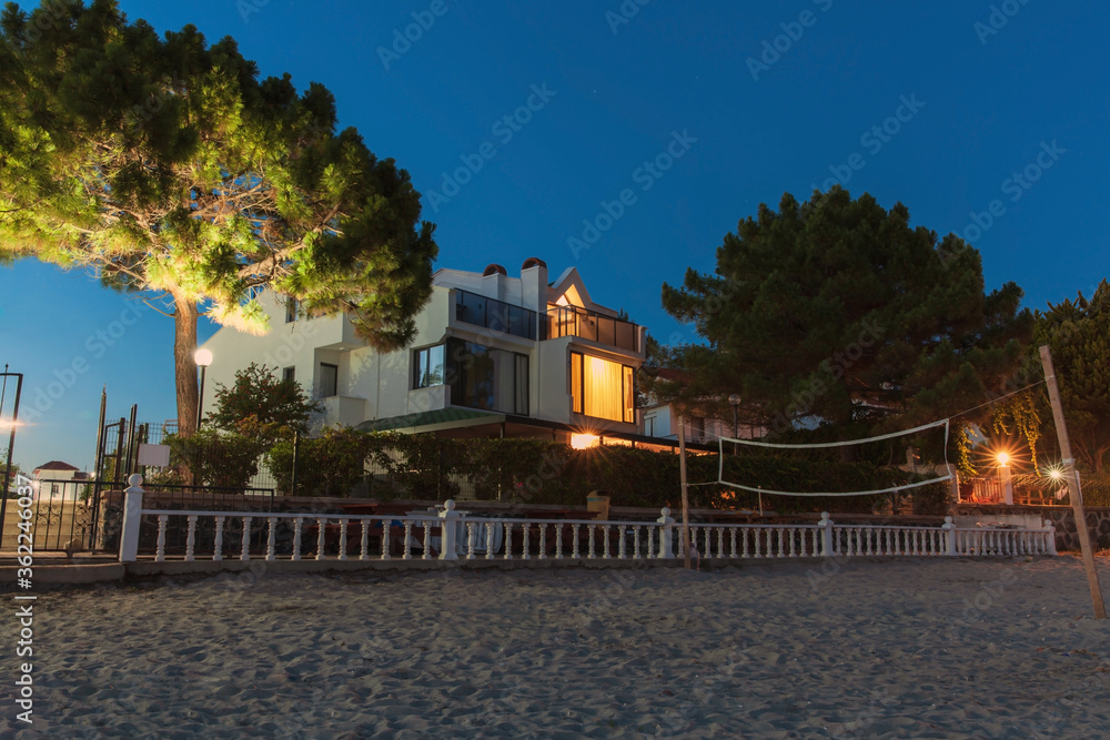 Home on the seaside. The view of a beach house at night with light in the window. 