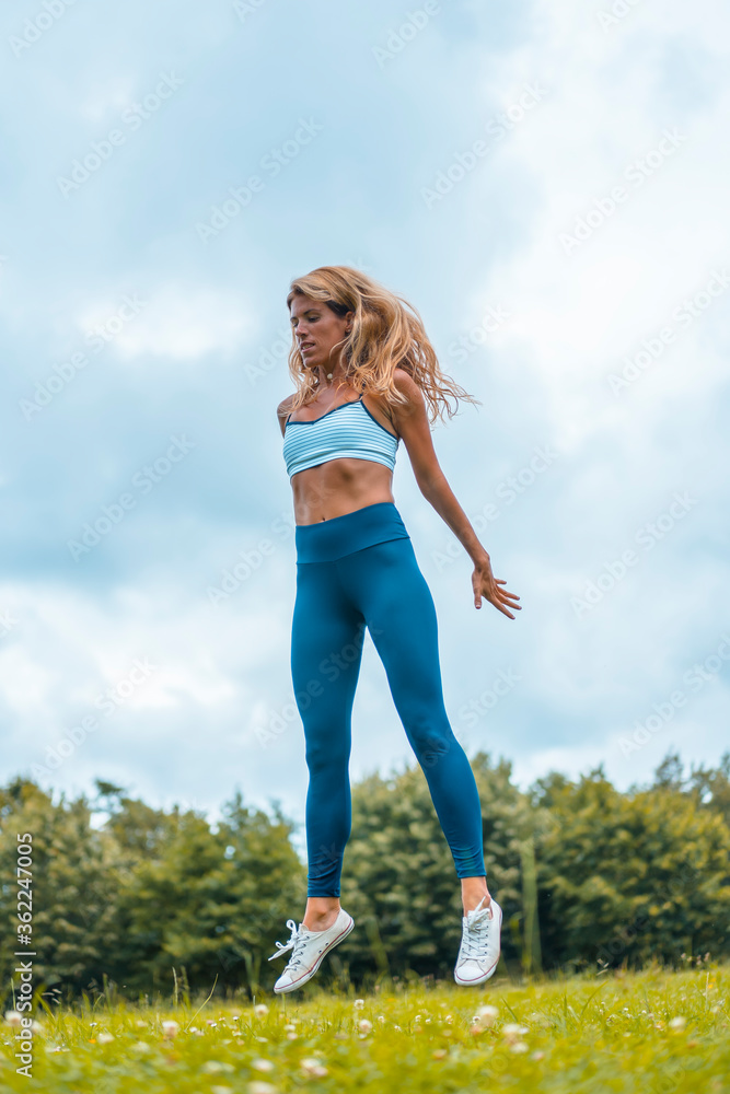 Fitness session with a young blonde caucasian woman exercising in nature with a blue maya on her feet and a white short shirt. Squatting and jumping Fitness session with a young blonde caucasian woman exercising in nature with a blue maya on her feet and a white short shirt. Squatting and jumping