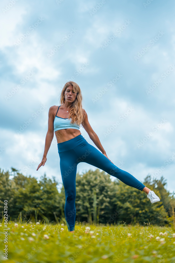 Fitness session with a young blonde caucasian woman exercising in nature with a blue maya on her feet and a white short shirt. Fitness session with a young blonde caucasian woman exercising in nature with a blue maya on her feet and a white short shirt.