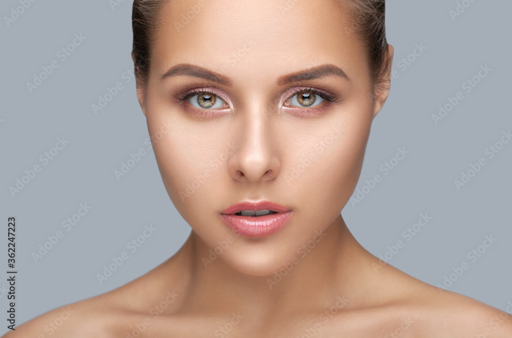 Portrait of a beautiful woman with brown hair, beautiful fresh make-up and with healthy clean skin on a gray background. Make-up and cosmetology concept. Portrait of a beautiful woman with brown hair, beautiful fresh make-up and with healthy clean skin on a gray background. Make-up and cosmetology concept.