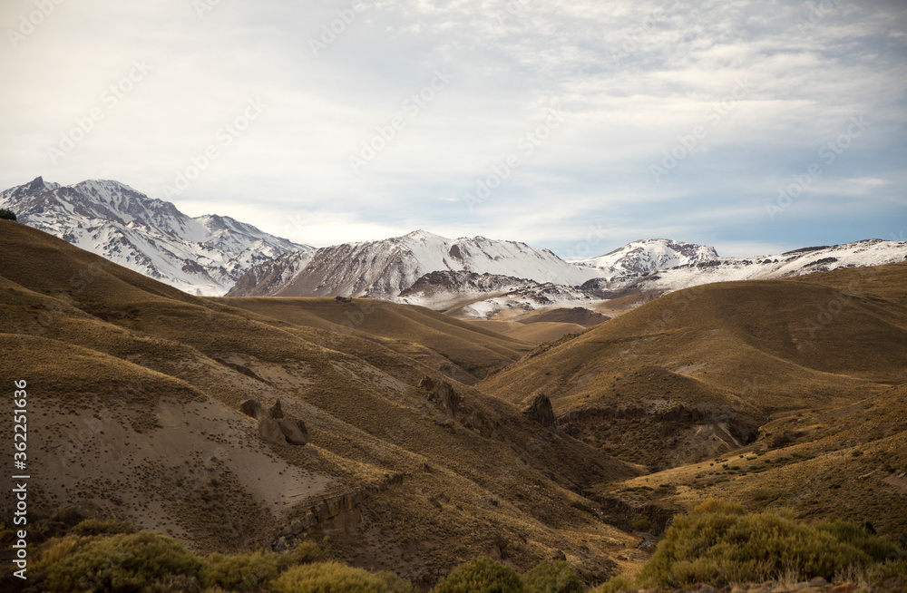Mountain range. View of a volcano, snowy peaks, valley, golden meadow, dunes and rocky formations. 