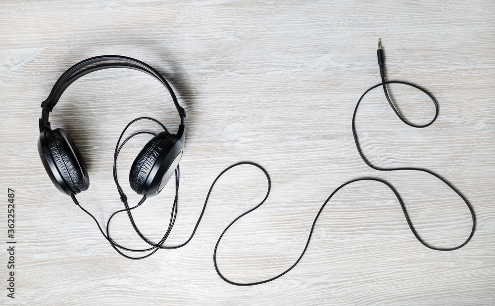 Black acoustic headphones on light wood table background. Top view. Flat lay. Black acoustic headphones on light wood table background. Top view. Flat lay.