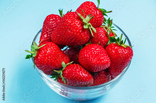 Many berries of ripe delicious strawberries lie in a glass bowl on a blue background. Background with strawberries. Summer berries. Healthy eating.