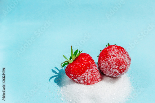 Two berries of ripe delicious strawberries lie on sugar on a blue background. Background with strawberries. Summer berries. Free space in the photo.