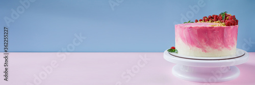 Celebratory cake with pink cream on a pink and blue background. Cake decor made from fresh raspberries, crushed pistachios and mint. Cake with raspberries. Great background with free space.