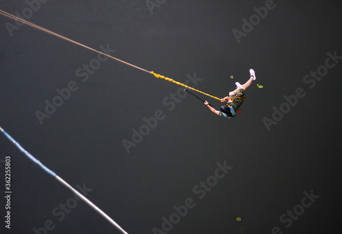 Concept of Extreme Sports and Fun. The man is a thrill-seeker and a rope jumper from the bridge. He is very happy to make a dream come true. He is holding an action camera and insanely happy