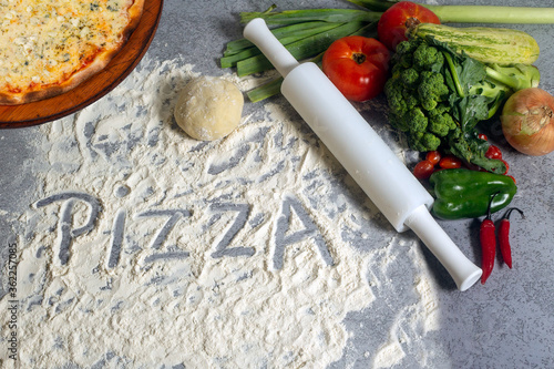 A  cheese pizza and raw pizza ingredients on the gray background. Pizza written with wheat flour. photo