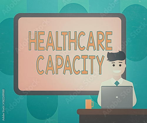 Handwriting text writing Healthcare Capacity. Conceptual photo maximum amount of patients provided with the right medical service Blank Bordered Board behind Man Sitting Smiling with Laptop Mug on photo