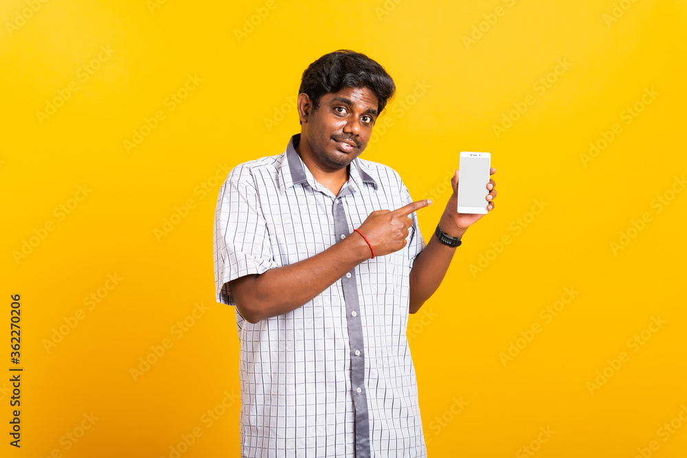 Asian happy portrait young black man smile standing wear shirt making finger pointing on smart digital mobile phone blank screen isolated, studio shot yellow background with copy space Asian happy portrait young black man smile standing wear shirt making finger pointing on smart digital mobile phone blank screen isolated, studio shot yellow background with copy space
