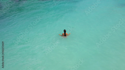 Aerial view of young beautiful woman in red bikini swimming in light blue azure turquoise water of sea, relaxing in ocean. Summer beach vacation. Malibu lifeguard Maldives Melasti beach Bali Indonesia