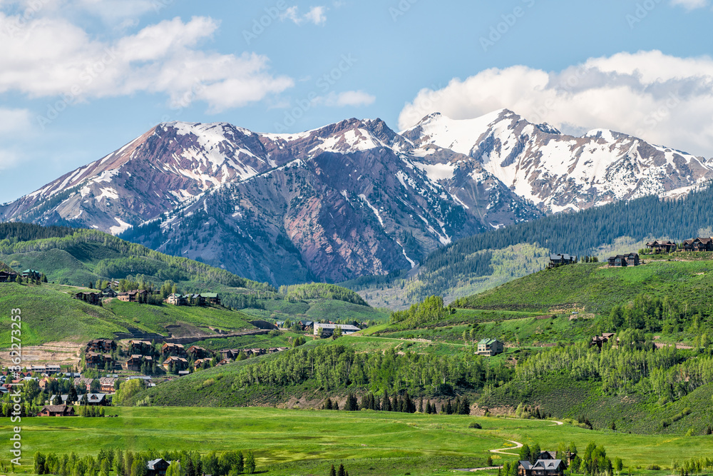 Mount Crested Butte mountain peak range and village in summer with lodging houses on hills with green grass open hill and snowcapped rocky mountains