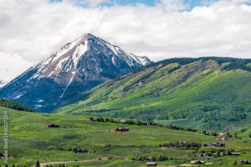 Mount Crested Butte mountain peak and village in summer with hotel lodging houses on hills with green grass meadow color and snowcapped rocky mountains