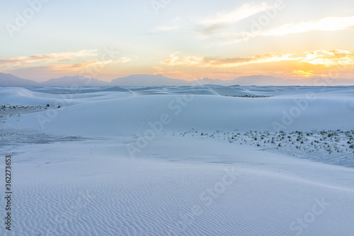 White sands dunes national monument park with sand patterns ripples on dune in New Mexico with sun over horizon at sunset and mountains silhouette