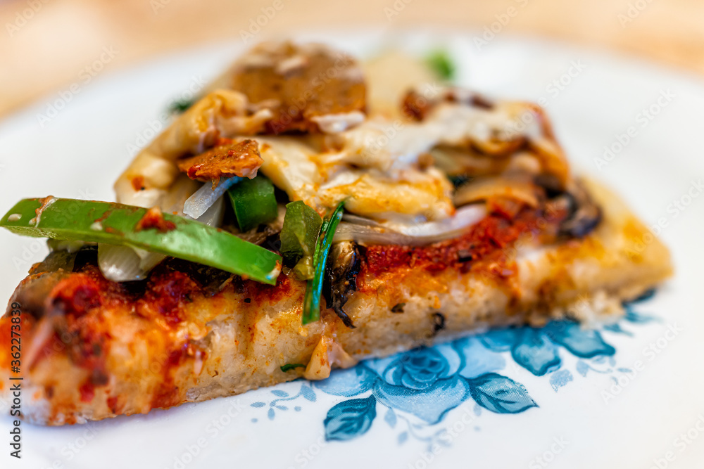 Homemade gluten free pizza slice cooked with tomato sauce, toppings of green bell peppers mushrooms and vegan sausage and melted cashew cheese on blue plate Homemade gluten free pizza slice cooked with tomato sauce, toppings of green bell peppers mushrooms and vegan sausage and melted cashew cheese on blue plate