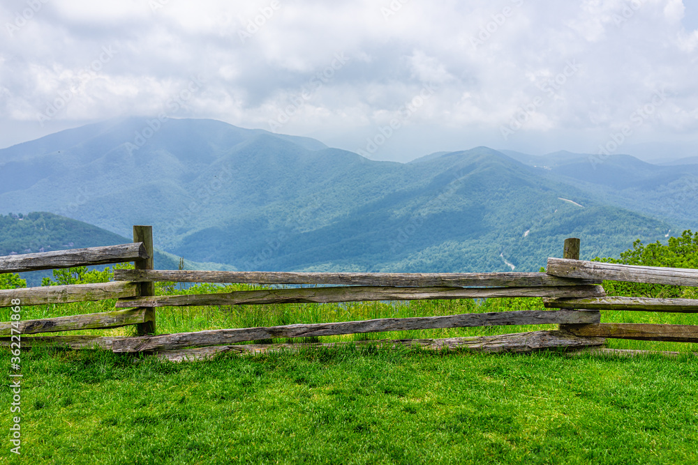 Devil's Knob Overlook green grass field meadow and fence at Wintergreen resort town village near Blue Ridge parkway mountains in summer clouds mist fog covering rolling hills