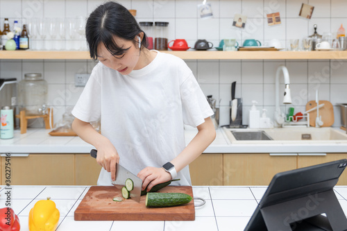 A pure girl playing tablet while cutting vegetables

