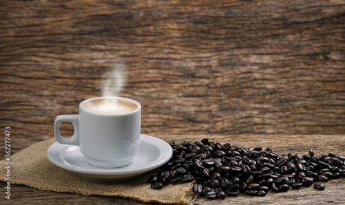 Coffee cup and coffee beans roasted in a sack on a wooden floor.