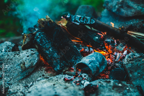 Vivid smoldered firewoods burned in fire close-up. Atmospheric warm background with orange flame of campfire and blue smoke. Wonderful full frame image of bonfire. Burning logs in beautiful fire.