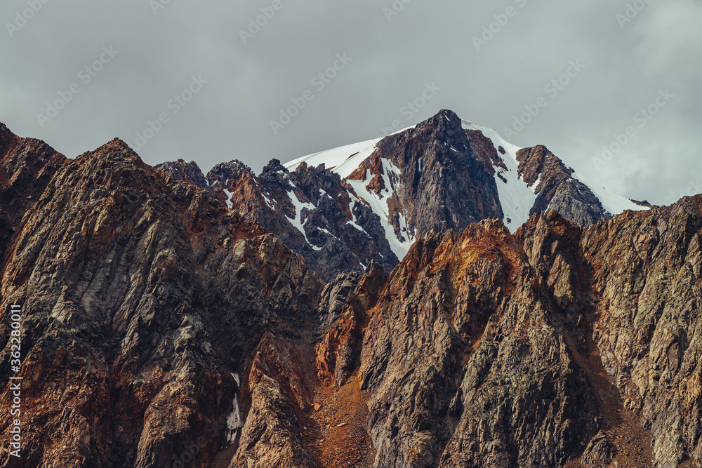 Awesome view to giant glacier on great pointed rock behind beautiful mountain with sharp stones on top under cloudy sky. Atmospheric highland scenery with great pointed rocky mountains in overcast day