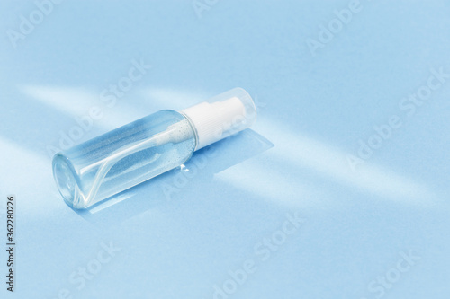 Small bottle with transparent cosmetic product, gel or crem on blue colored background. Flack with moisturizer for self-care. Monochrome image.
