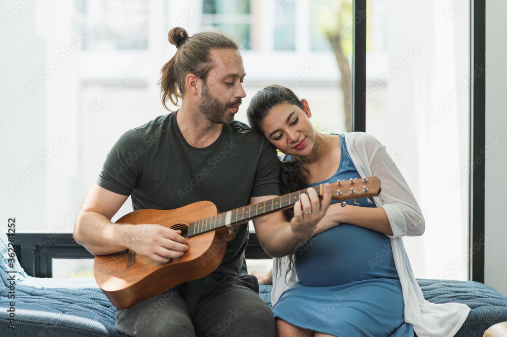 The man played the guitar for his wife to listen. She is pregnant They were all together in the house on the sofa. Family couple concept. The man played the guitar for his wife to listen. She is pregnant They were all together in the house on the sofa. Family couple concept.