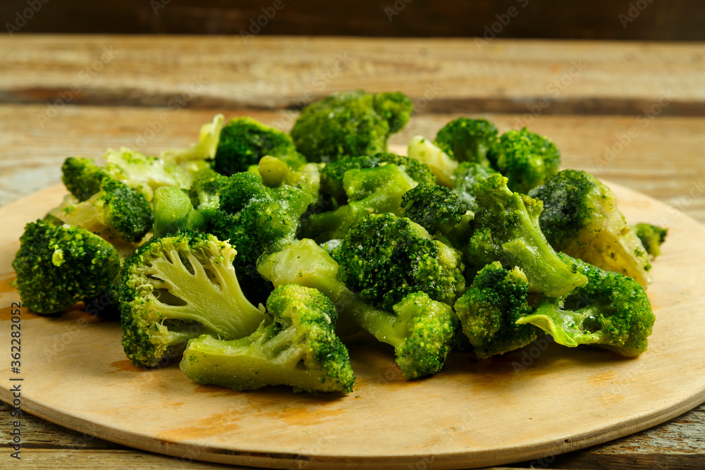 Scattered frozen broccoli on a round wooden board.