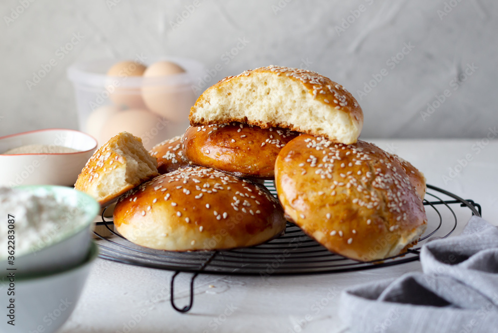 Buns covered with sesame seeds on baking grid and ingredients