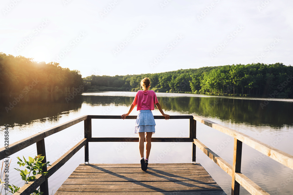 Woman on wooden bridge near lake on green nature background.
