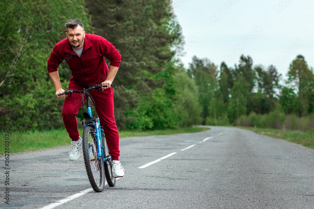 A man in a tracksuit on a bicycle rides on a road in the forest. The concept of a healthy lifestyle, cardio training. Copyspace.