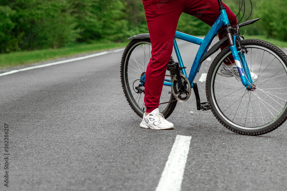 Fototapeta premium Legs on the pedals of a bicycle close-up, riding a road in the forest. The concept of a healthy lifestyle, cardio training. Copyspace.