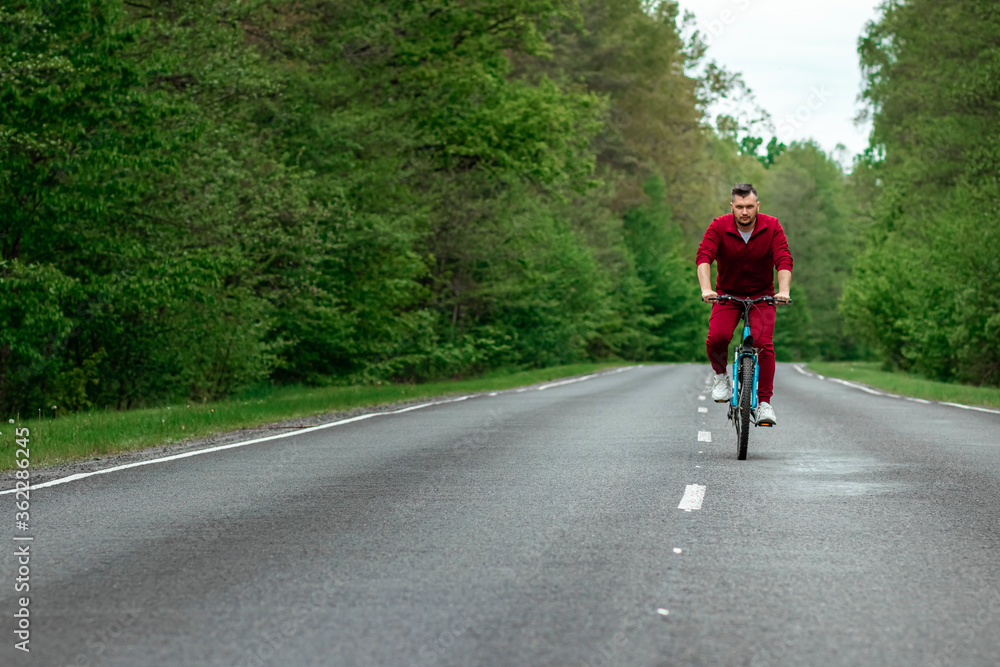 A man in a tracksuit on a bicycle rides on a road in the forest. The concept of a healthy lifestyle, cardio training. Copyspace. A man in a tracksuit on a bicycle rides on a road in the forest. The concept of a healthy lifestyle, cardio training. Copyspace.
