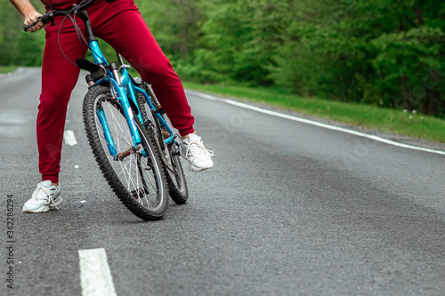 A man in a tracksuit stands next to a bicycle on a road in the forest. The concept of a healthy lifestyle  cardio training. Copyspace.