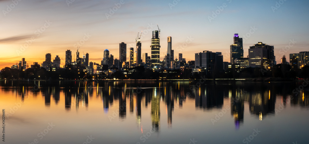 Naklejka premium The reflections of the melbourne city skyline at dusk in the still water of albert park lake