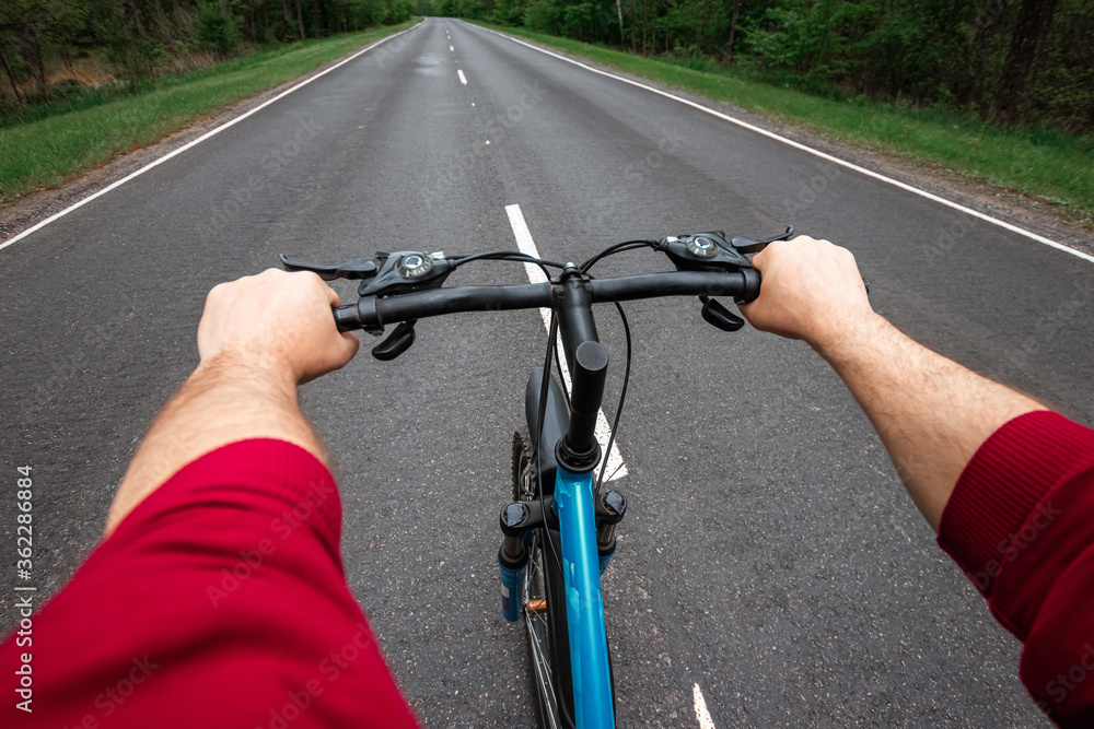 Male hands on the handlebars of a bicycle riding on a road in the forest. The concept of a healthy lifestyle, cardio training. Copyspace.