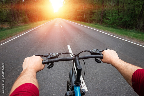 Male hands on the handlebars of a bicycle riding on a road in the forest. The concept of a healthy lifestyle, cardio training. Copyspace.
