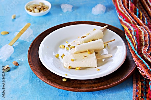 Photography Three portions of the Indian kulfi ice cream with cardamom and pistachios on a white plate on a blue background concrete