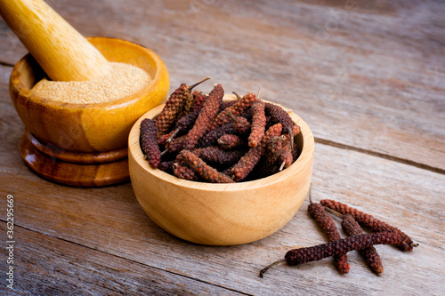 Dry Idian long pepper ( Piper Longum ,Piper retrofractum ) in wooden bowl and ground long pepper powder in wooden mortar isolated on wood table background. Herbs and medicine plant concept. photo