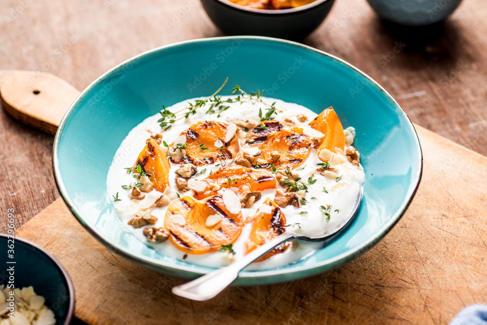 Breakfast bowl with grilled apricots with natural yoghurt, walnuts, almonds and thyme. Wodden background.