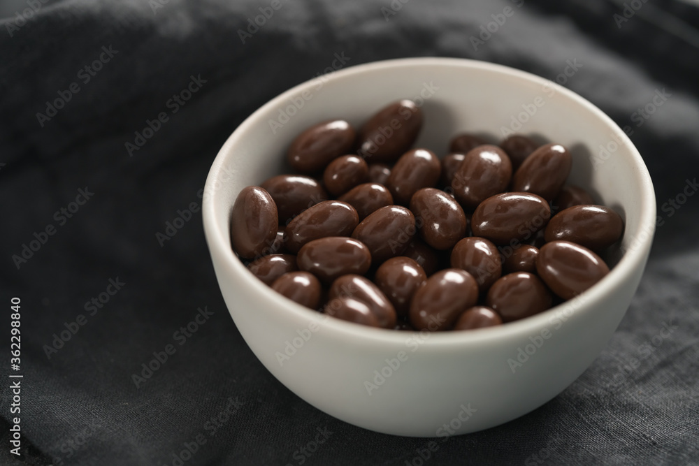 Milk chocolate dragee in white bowl on linen background Milk chocolate dragee in white bowl on linen background