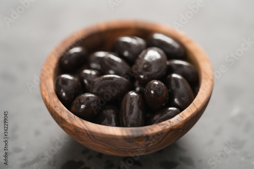 Dark chocolate dragee in olive wood bowl on concrete background