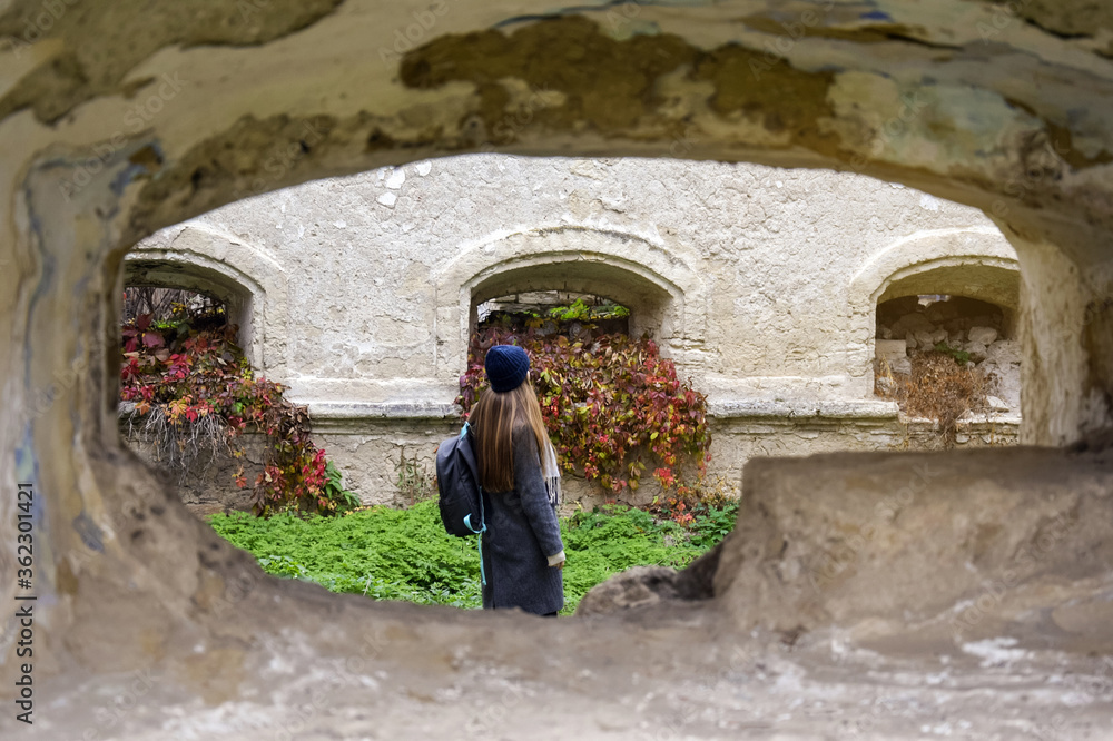 Vacation, travel, tourism in autumn season. Young girl with long blond hair and backpack examines the ruins of an ancient building.