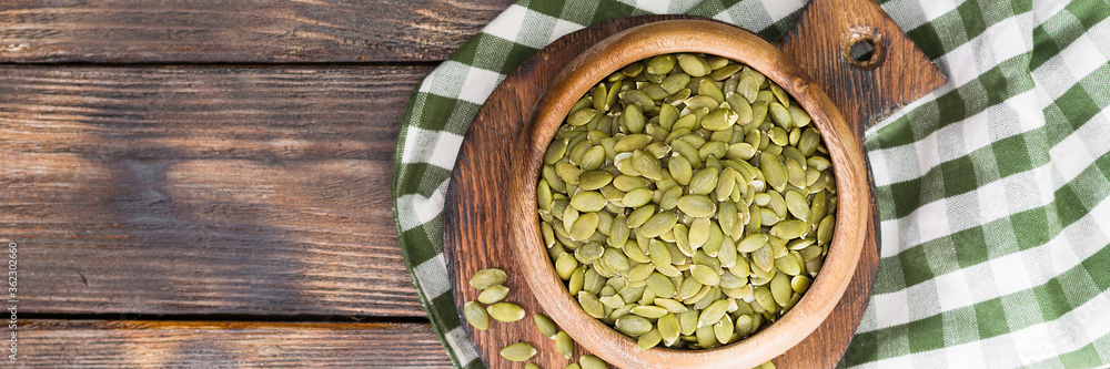 Pumpkin seeds in a wooden bowl on a wooden table. Lots of pumpkin seeds in a bowl close-up. The view from the top. Banner with space for text