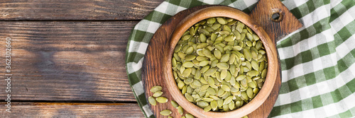Obraz na płótnie Pumpkin seeds in a wooden bowl on a wooden table. Lots of pumpkin seeds in a bowl close-up. The view from the top. Banner with space for text w salonie