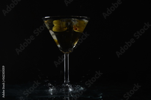 Martini with olives. Splashes near glass of cocktail. Black background