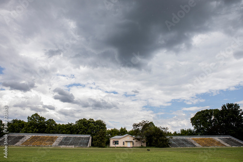 football field with empty seats, green grass and cloudy sky