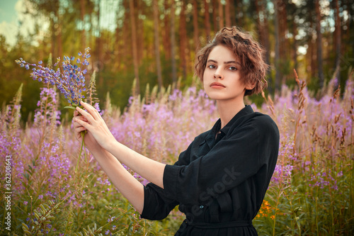 A young girl stands iin a blooming field of Ivan-tea with a bouquet of flowers. photo