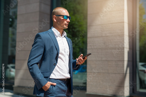 handsome young man in a summer suit on a walk in sunglasses with a phone in his hand